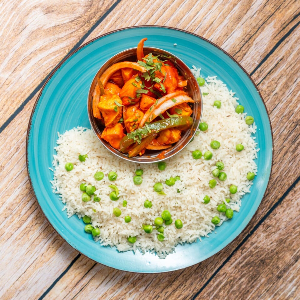 A vibrant Indian dish with paneer, onions, and peppers in a bowl, surrounded by rice and peas.