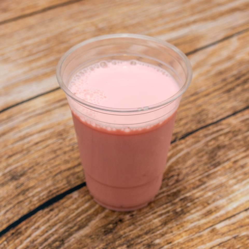Pink frothy drink in a clear plastic cup on a light brown wooden table.