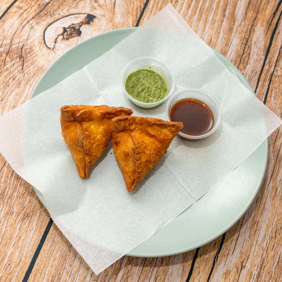 Two golden-brown samosas with green and brown dipping sauces on a light green plate.