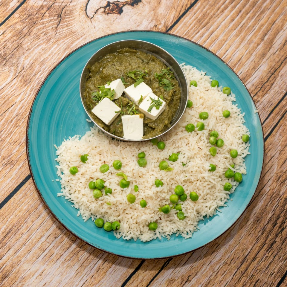 Palak Paneer with white rice and green peas on a blue plate, on a wooden surface.