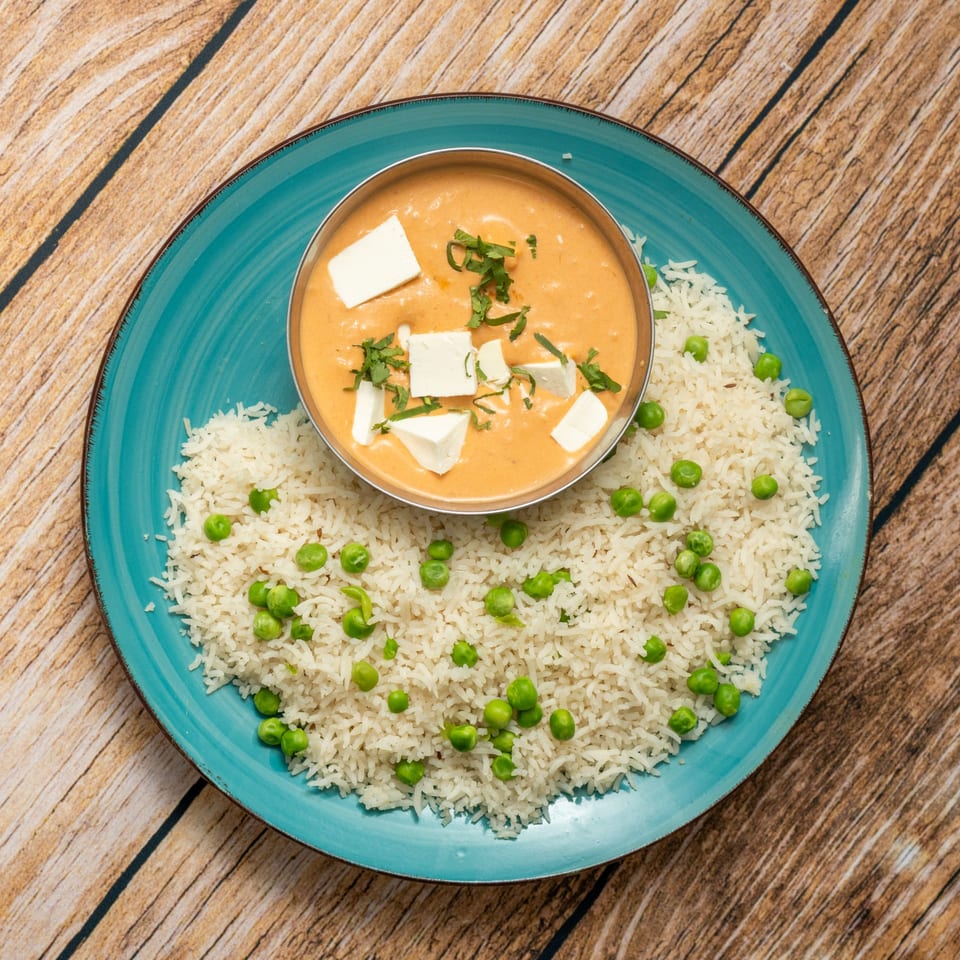 A teal plate with a bowl of paneer butter masala and a side of rice with green peas.