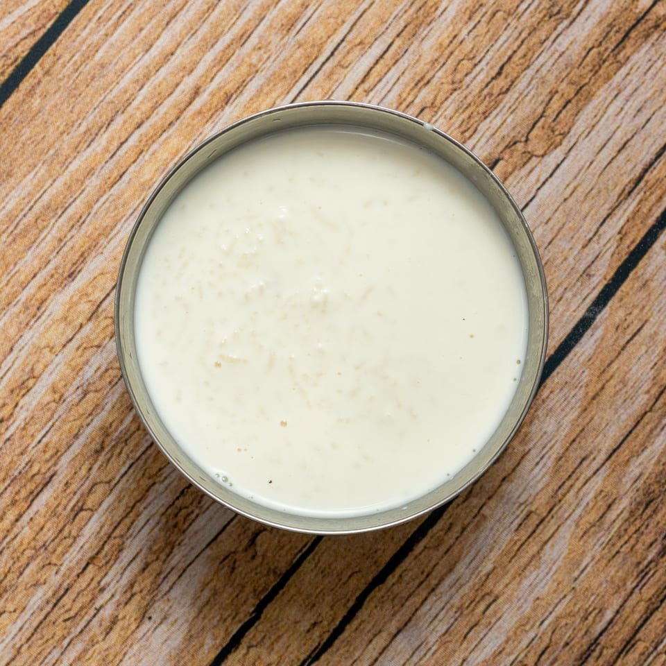 Overhead shot of a metal bowl filled with creamy white rice pudding on a wooden table.