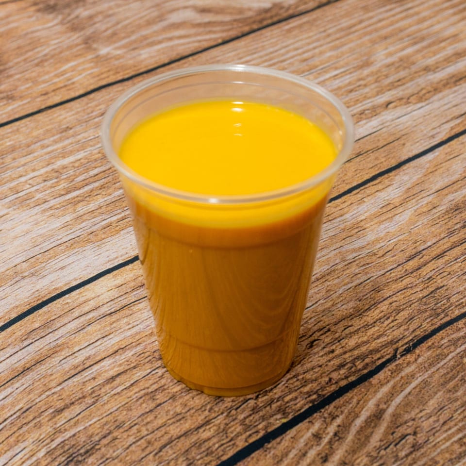A plastic cup filled with a vibrant orange and yellow layered drink sits on a wooden surface.