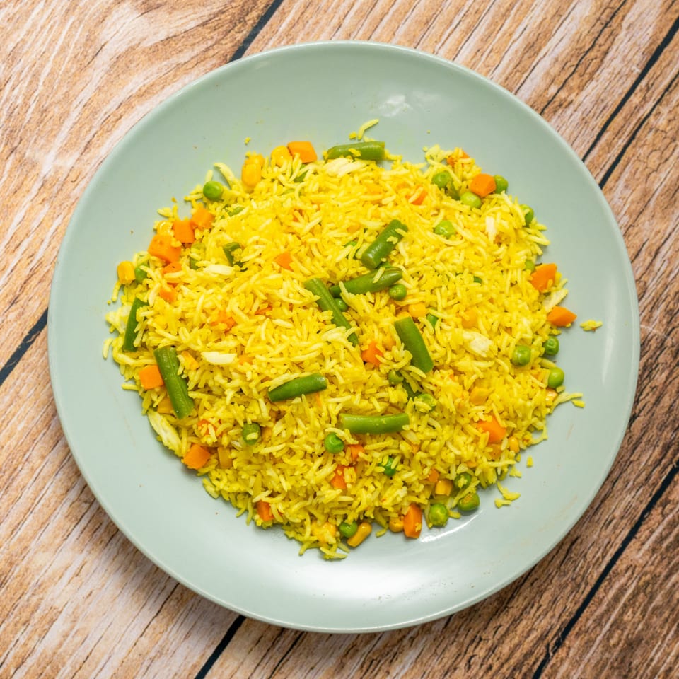 Bright yellow vegetable fried rice with carrots, peas, corn, and green beans on a light blue plate.
